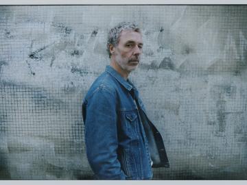 Le chanteur Baxter Dury se tient de profil, il porte une veste en jean.